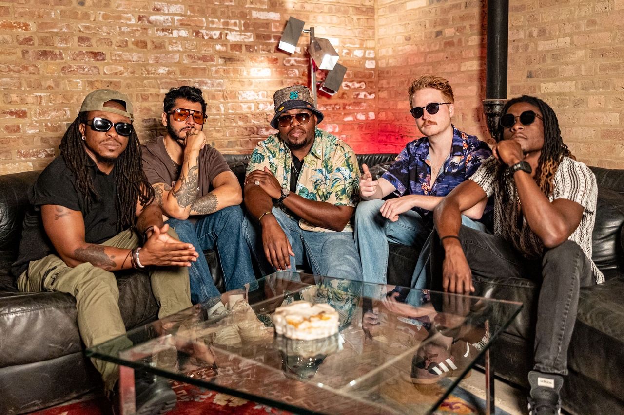The five members of Hot Like Mars on a black leather couch against a brick wall